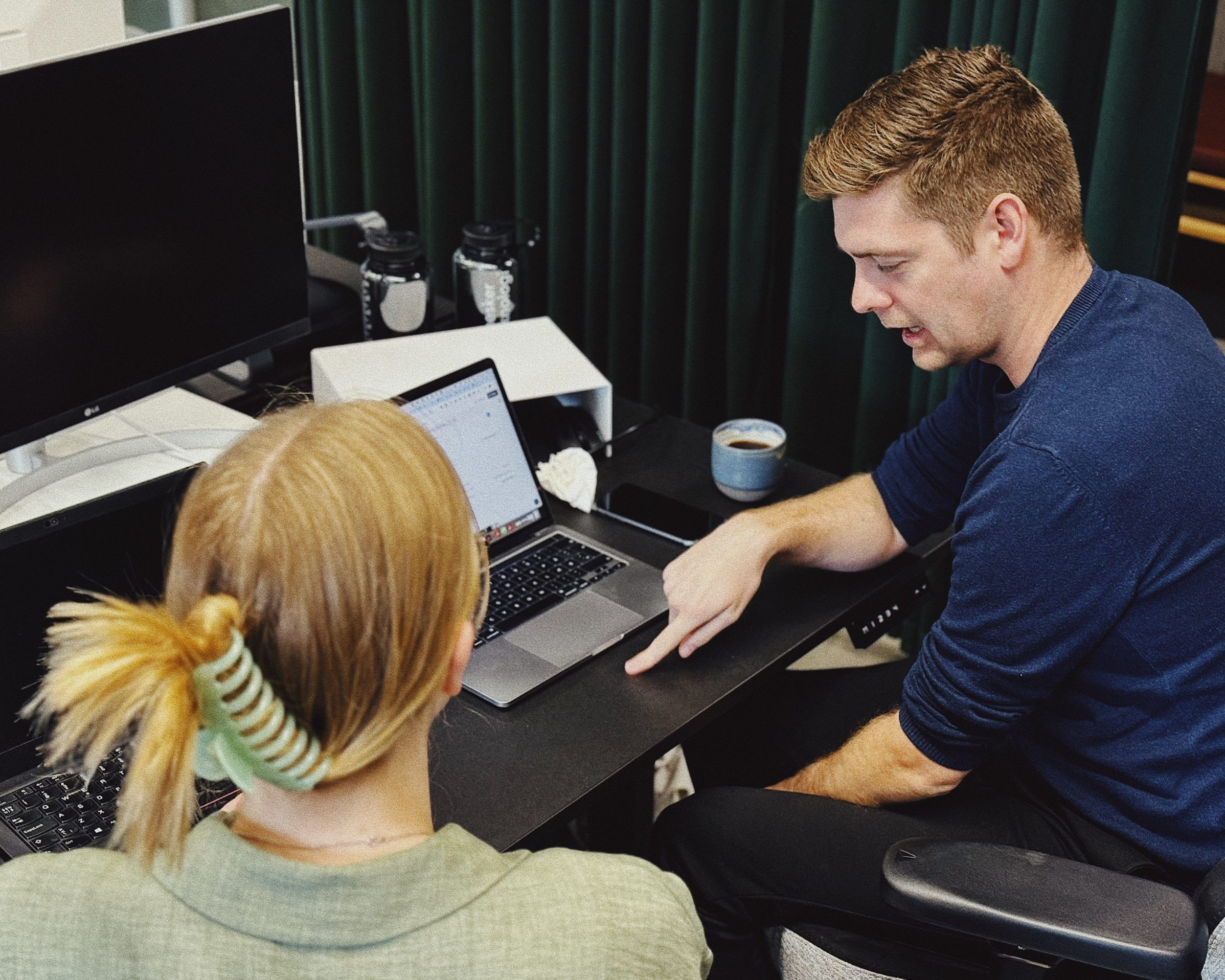 To personer arbejder sammen ved en bærbar computer på et skrivebord